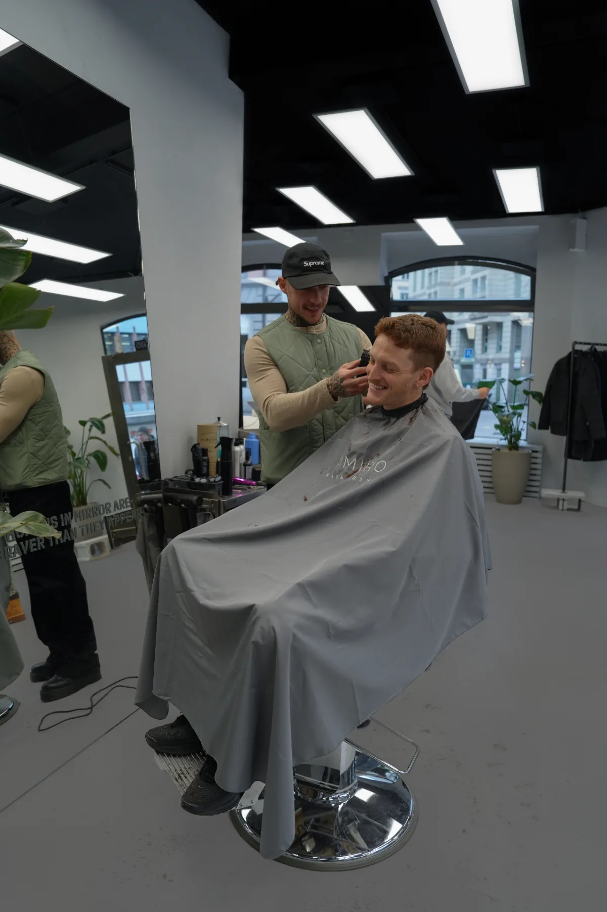 Brand photograph of a barber giving a haircut to a smiling client in a modern barbershop.