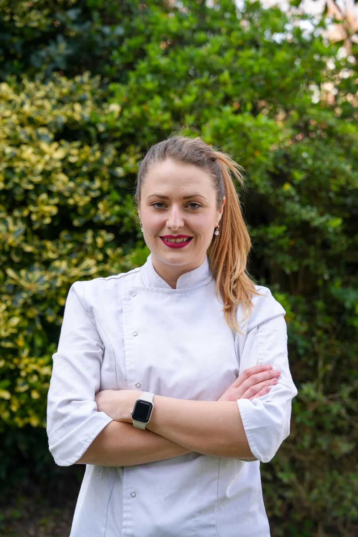 Close portrait of a chef standing outdoors with folded arms against a green garden background.
