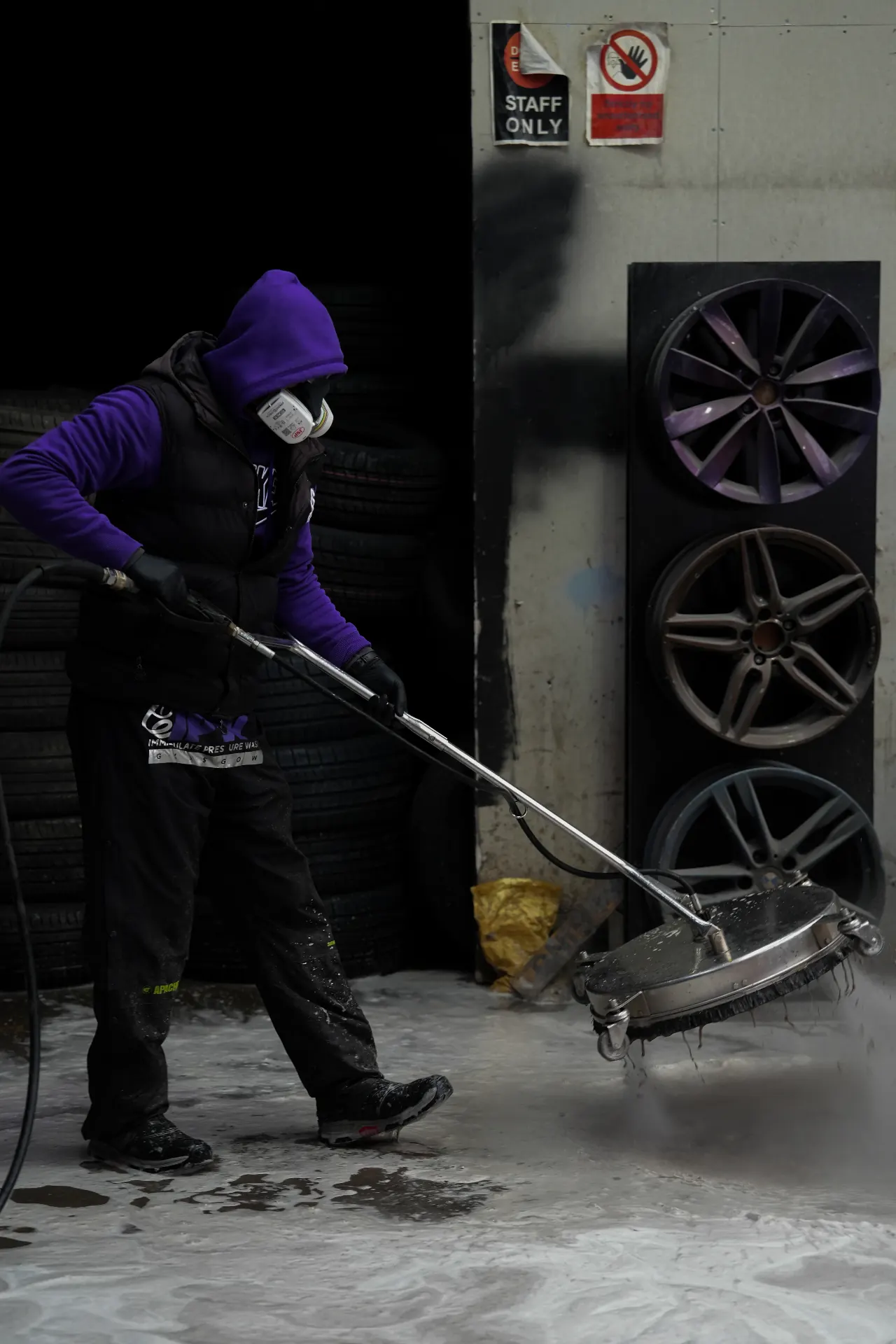 Commercial detail photograph of a worker pressure cleaning beside displayed wheels in an industrial workspace.